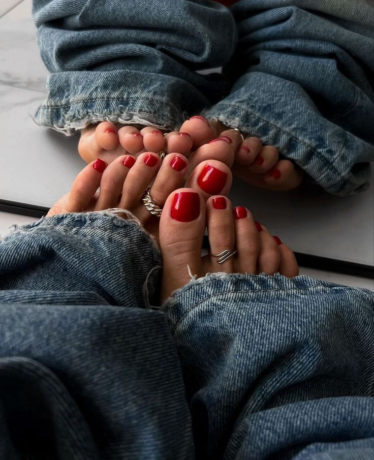 Feet with red nail polish and toe rings, wearing denim jeans