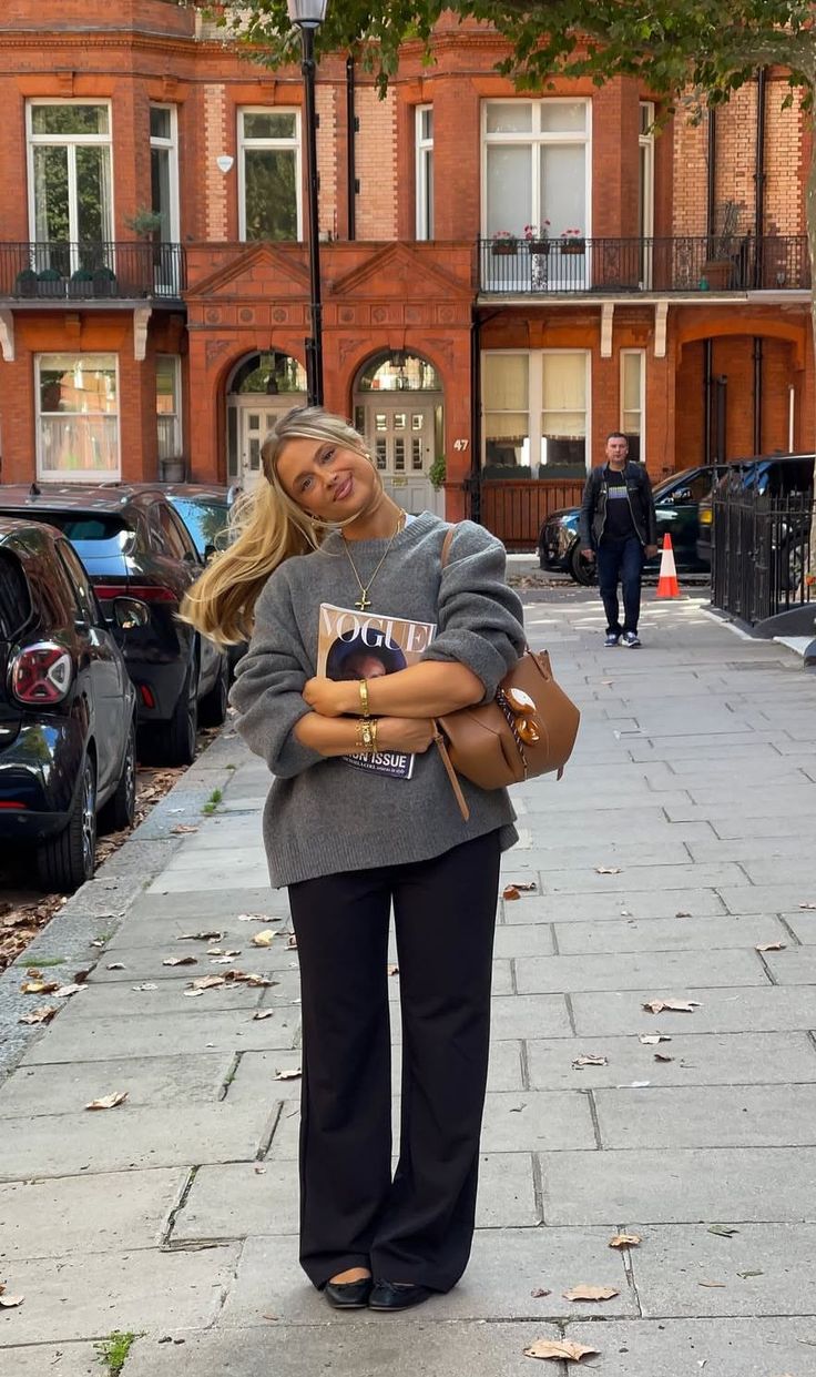 Woman with blonde hair in a gray sweater and black pants on a city street