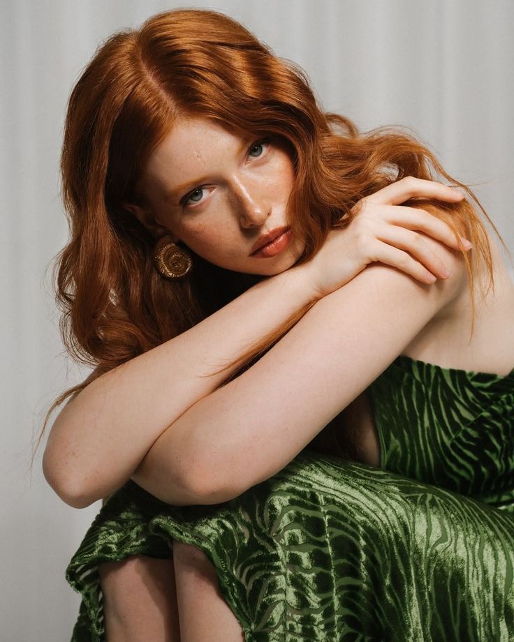 Woman with red hair and freckles wearing a green velvet dress and gold earrings