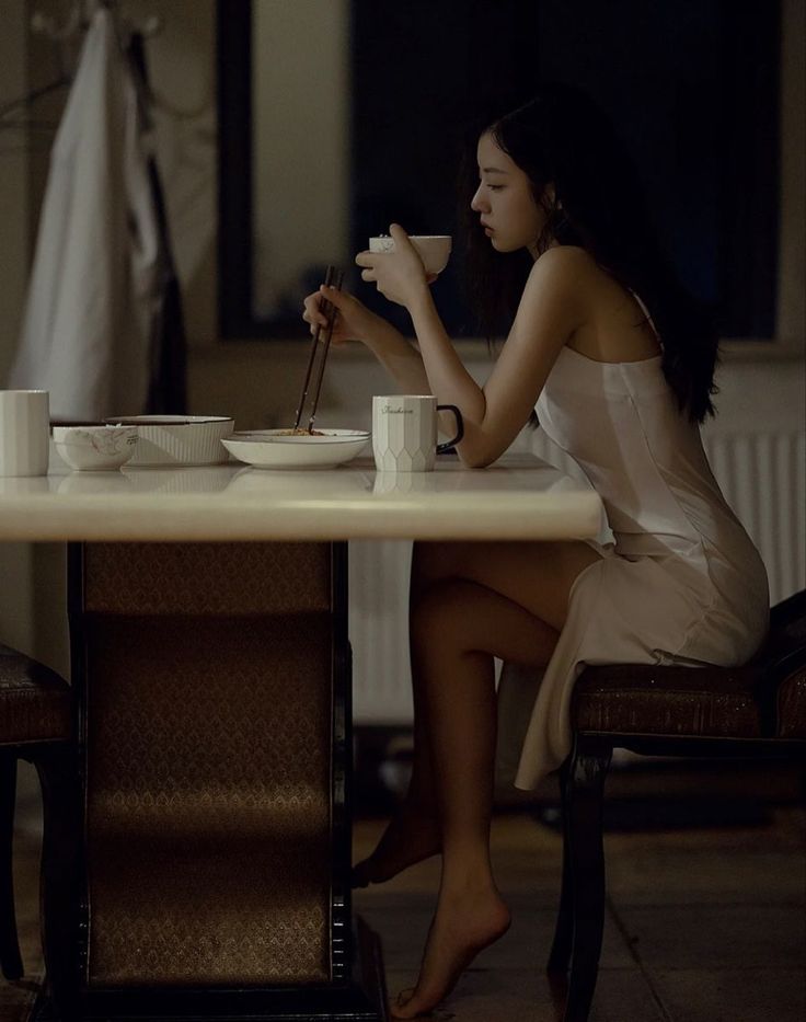 Woman with long dark hair eating at a table in soft, dark lighting
