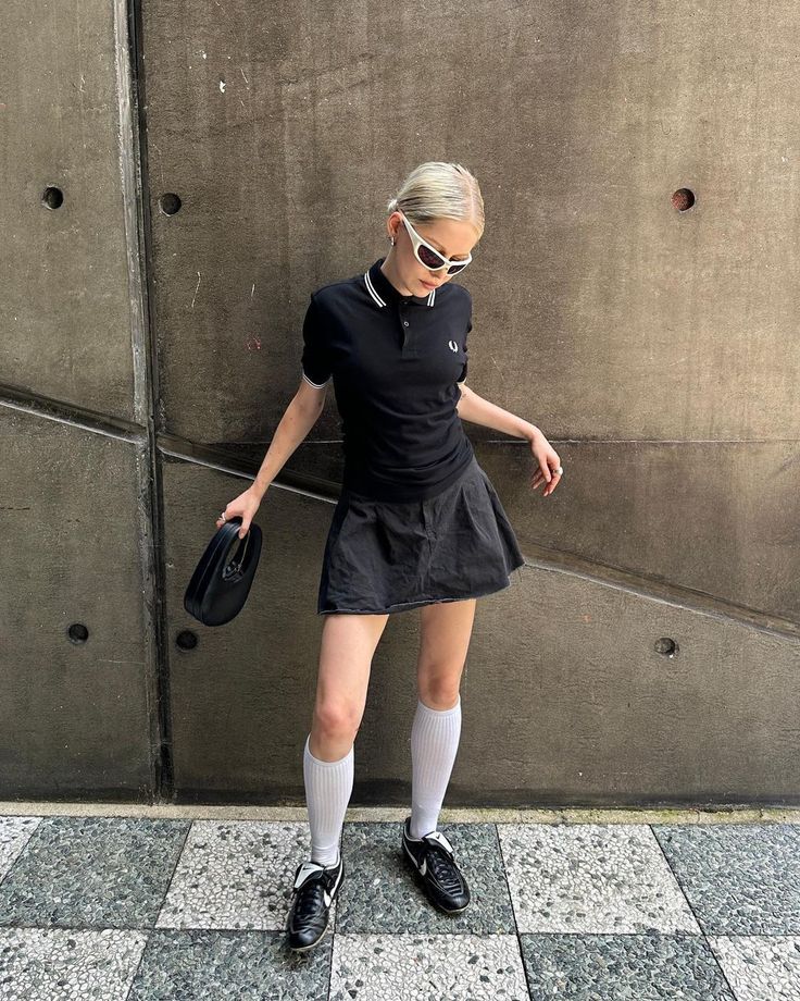 Woman in a black polo shirt and mini skirt with white knee socks and sunglasses