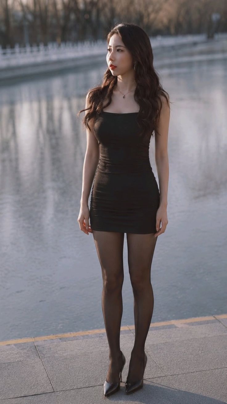 Woman in a black dress and pantyhose standing outdoors by water