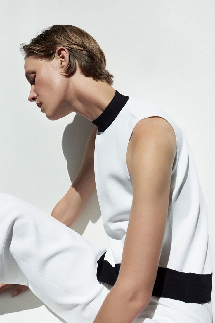 Woman with short hair wearing a white top with a black collar and white pants