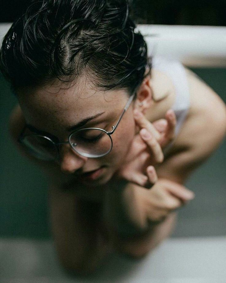 Person with wet black hair and glasses looking down in soft indoor lighting