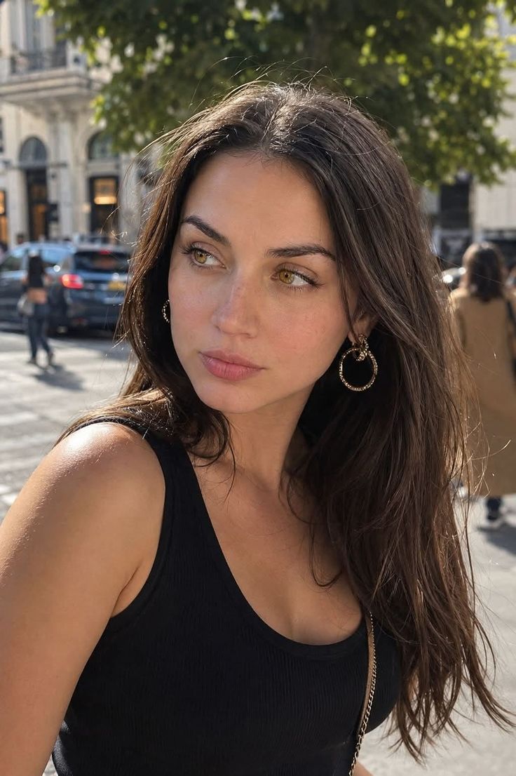 Woman with long brown hair and hoop earrings in a black tank top outdoors