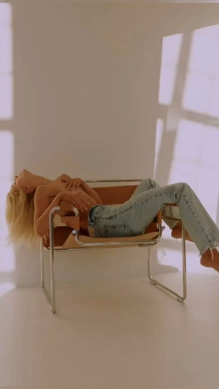 Blonde woman in blue jeans reclining on a chair with exposed skin