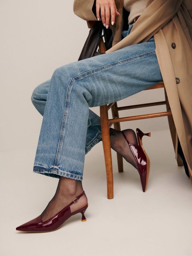 Person in blue jeans, a trench coat, and red kitten heels sitting on a chair