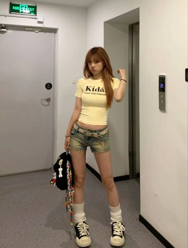 Woman in a yellow crop top and denim shorts standing indoors