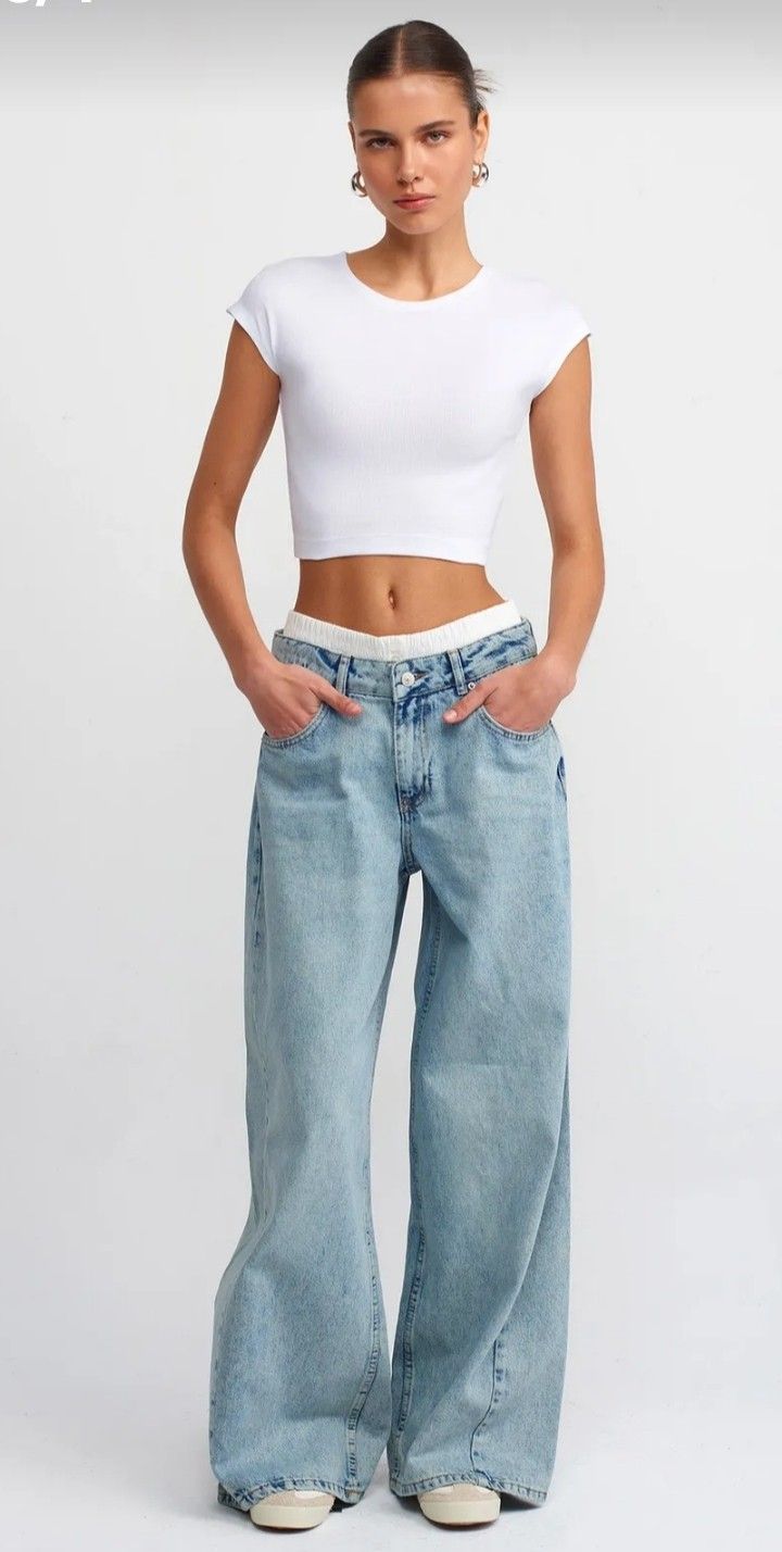 Woman in a white crop top and baggy light wash jeans with hands in pockets