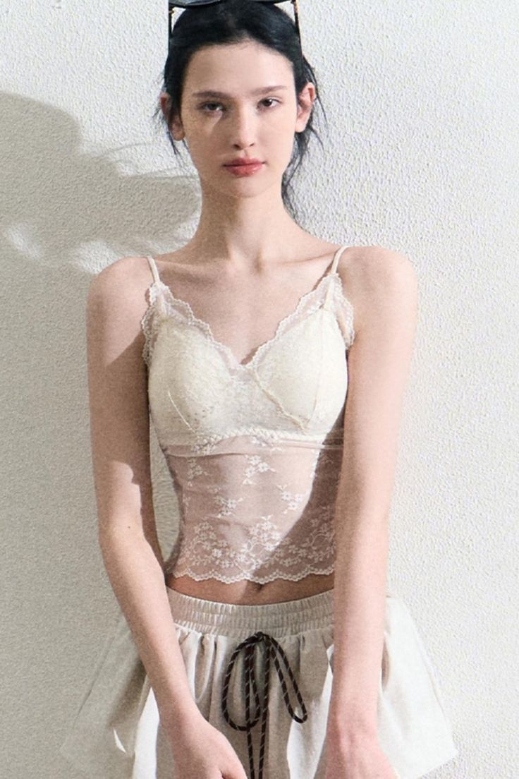 Woman in a lace top and shorts against a white wall