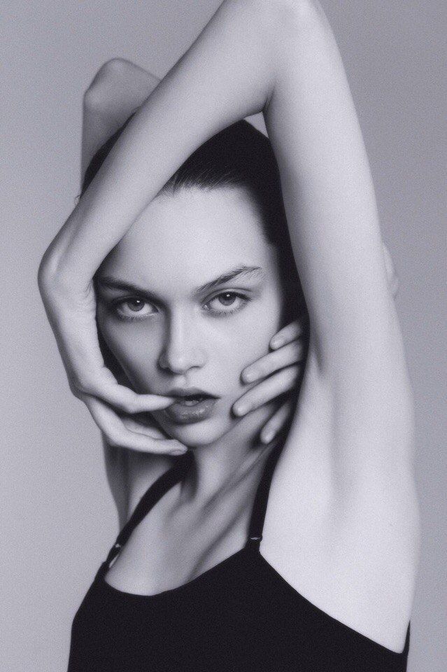 Woman in a black top with hands framing her face in a provocative pose