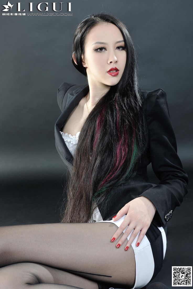 Woman with long black hair and red lipstick in a black blazer and white top