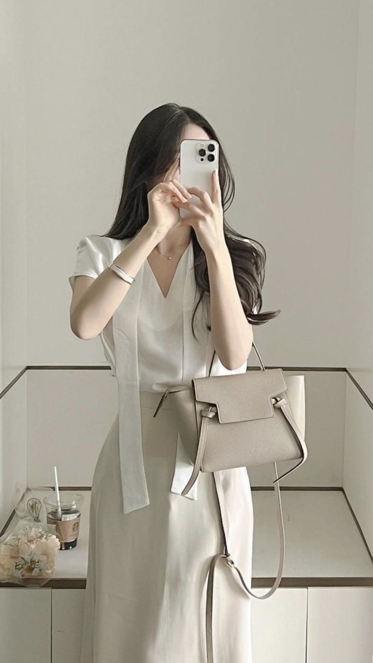 Woman in a white blouse and beige skirt taking a mirror selfie