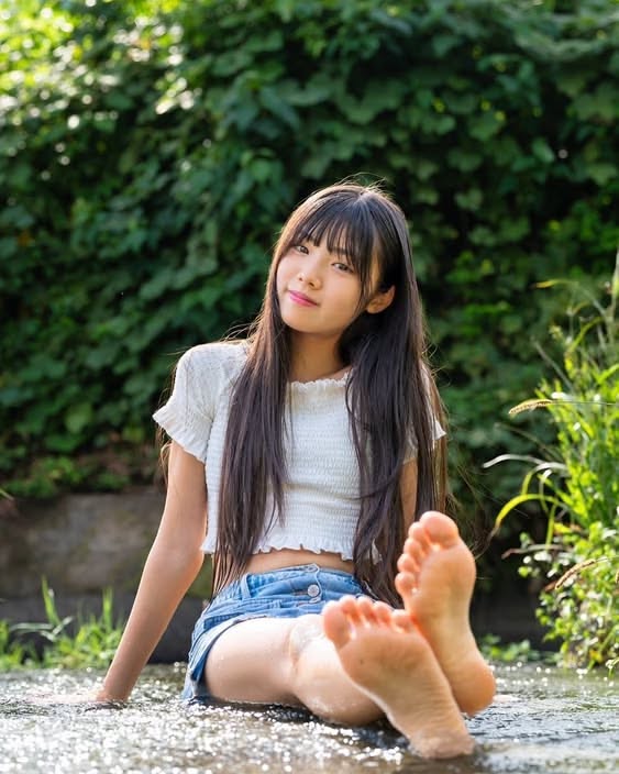 Young woman with long hair and denim shorts sitting in shallow water outdoors