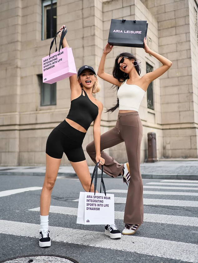 Two women in athletic wear holding shopping bags on a city street