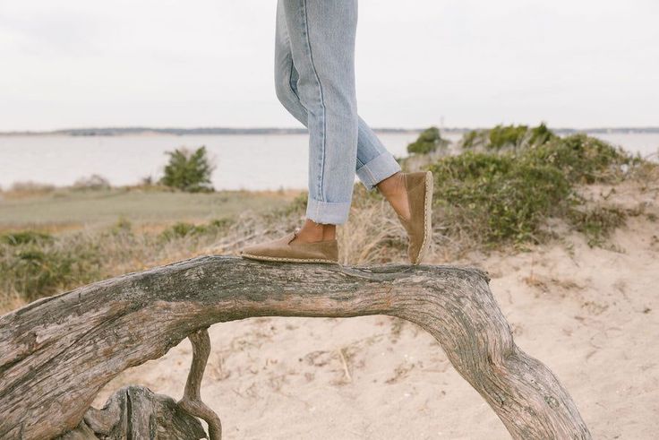 Person in jeans and barefoot shoes walking on driftwood on a sandy beach