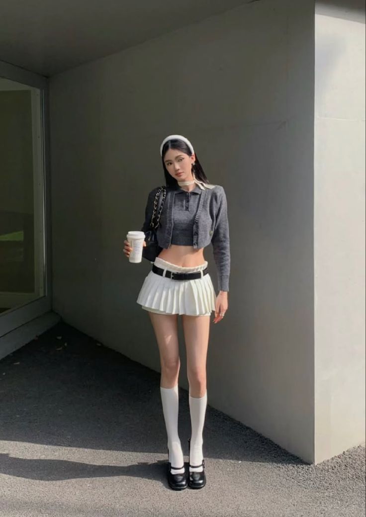 Woman in a white pleated skirt and crop top holding a coffee cup outdoors