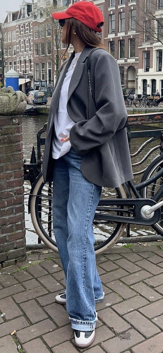 Person in a red cap and oversized blazer standing by a canal in a city