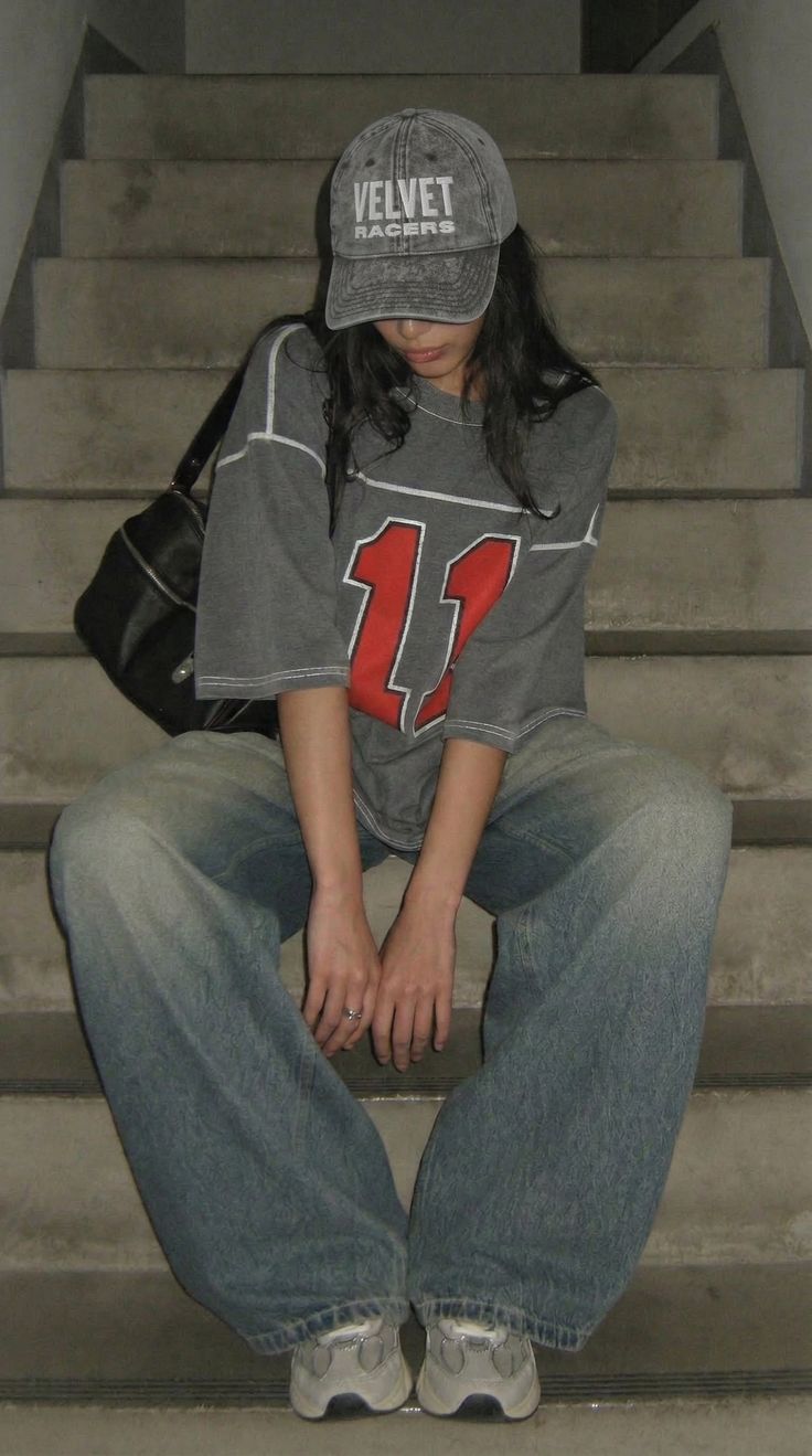 Person in a baseball cap and baggy clothes sitting on concrete stairs