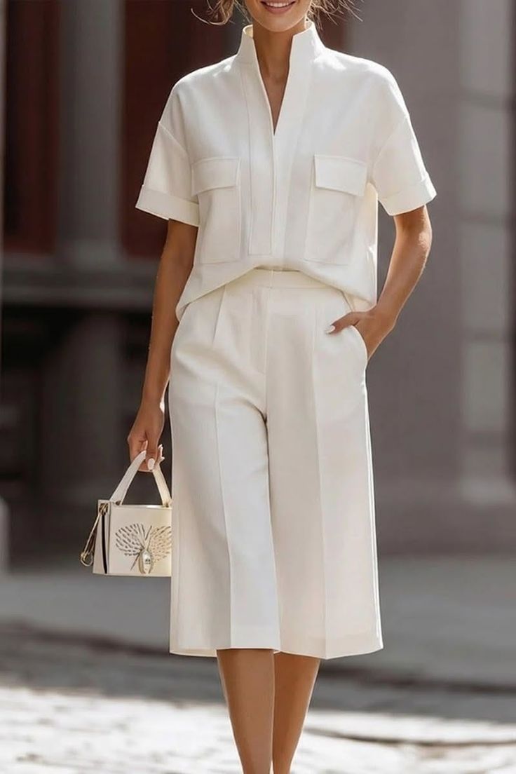 Woman in a white short-sleeve shirt and culottes holding a small handbag