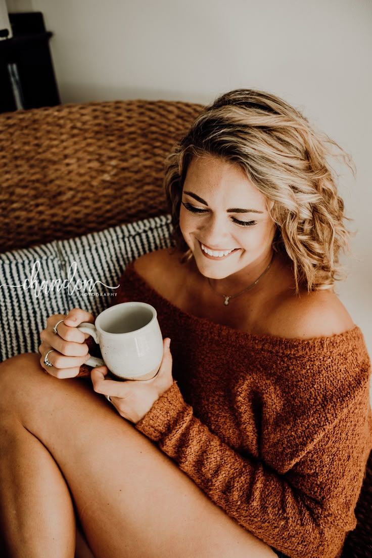 Woman with blonde curly hair in an off-shoulder sweater holding a mug