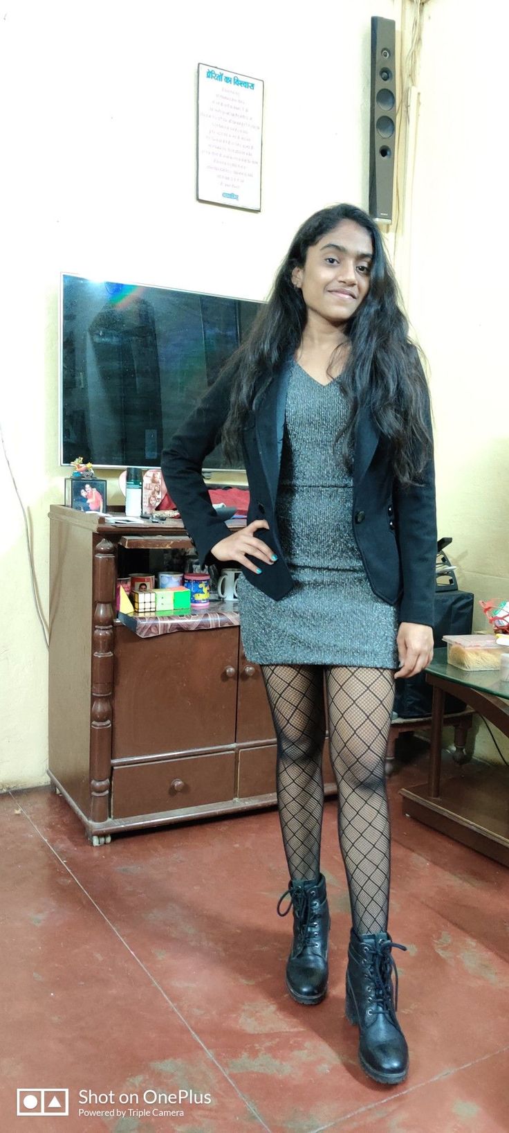 Woman in a black blazer, mini dress, and fishnet stockings posing indoors