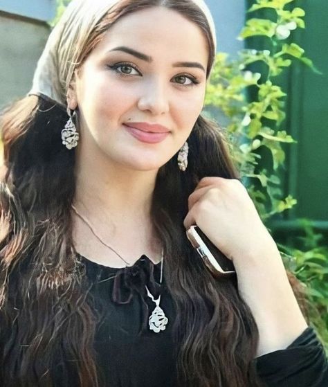 Woman with long dark hair and a head scarf wearing jewelry outdoors