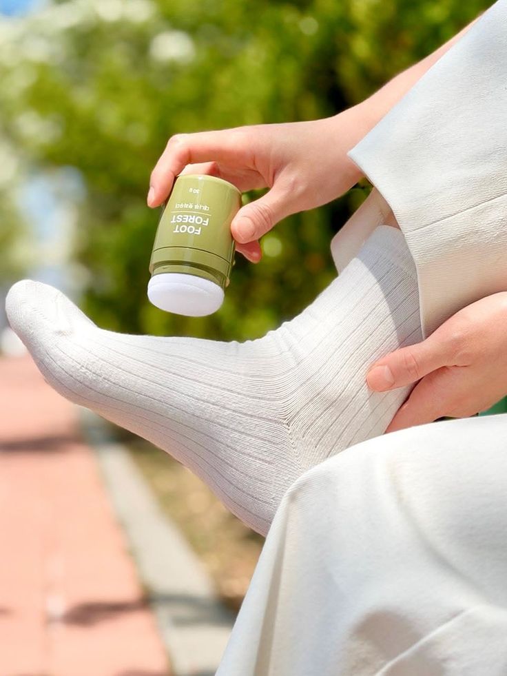 Person applying foot care product to a foot wearing a white sock outdoors