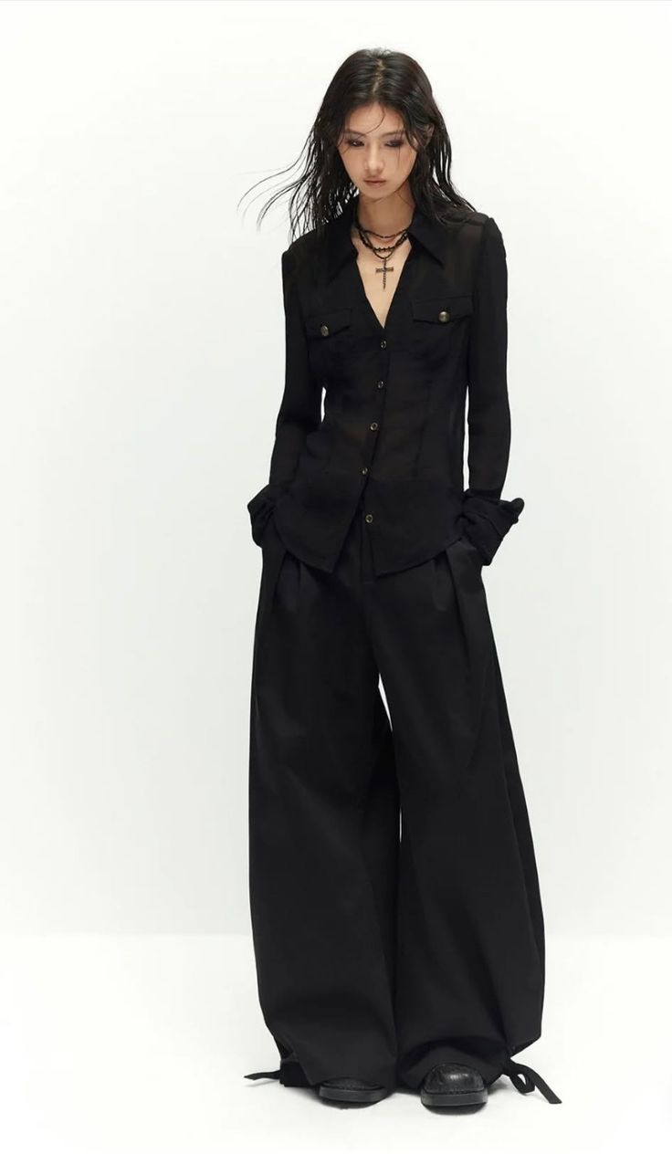 Woman in a black shirt and wide leg pants with a cross necklace