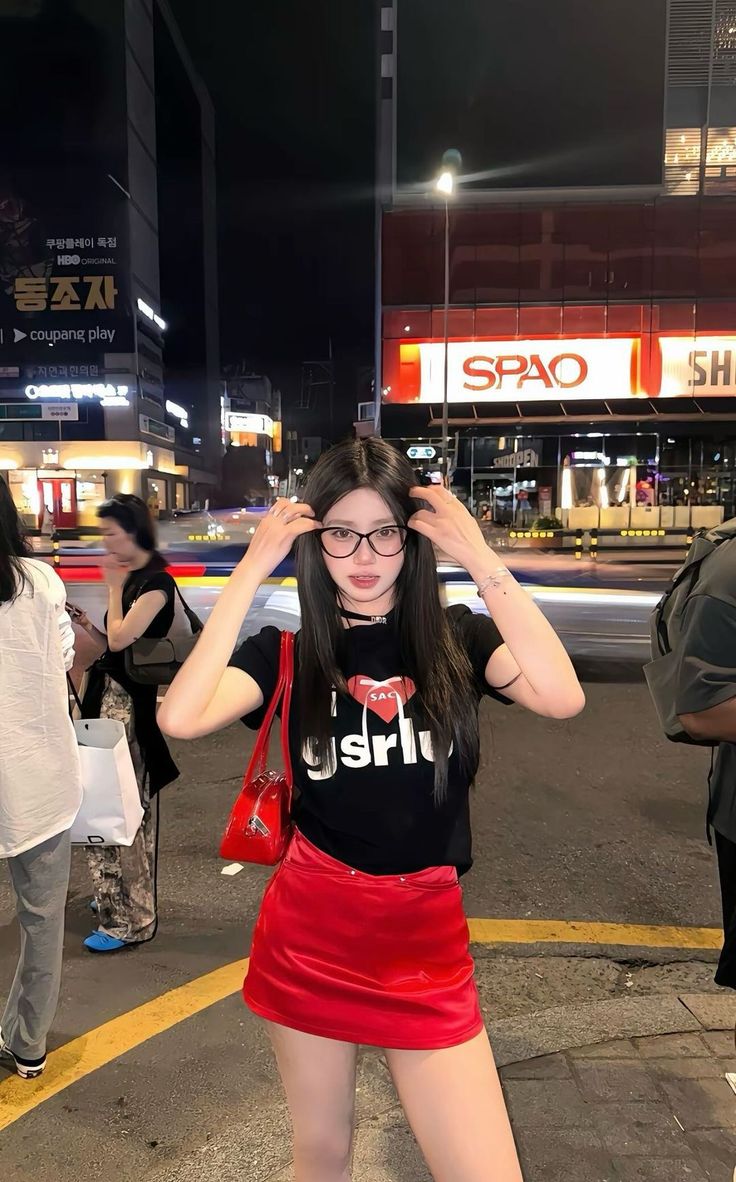 Woman in a red skirt and black t-shirt on a city street at night