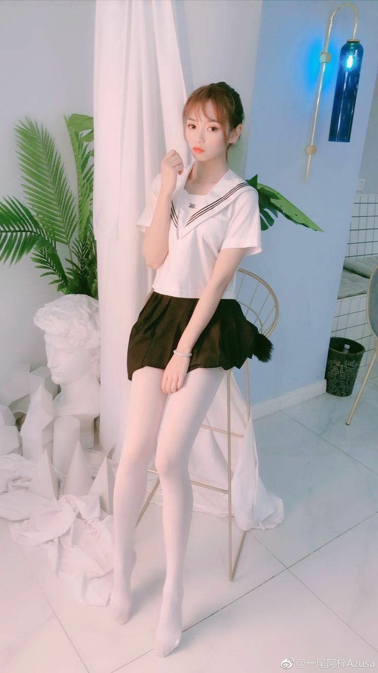 Woman in a school uniform and white tights sitting on a chair indoors