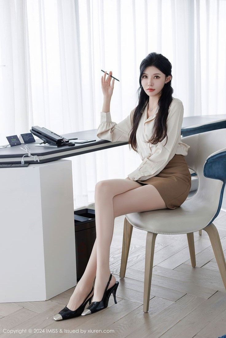 Woman with long black hair wearing a blouse and mini skirt, sitting indoors