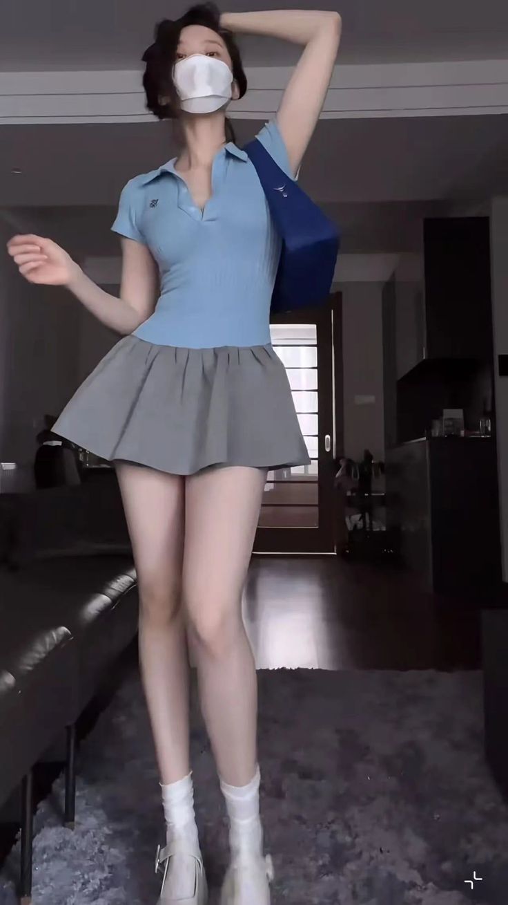 Woman in a blue polo shirt and pleated skirt wearing a face mask indoors