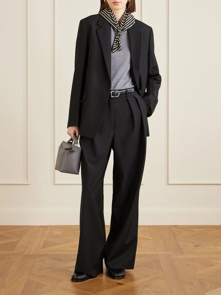 Person in a black suit with a striped scarf and gray handbag indoors
