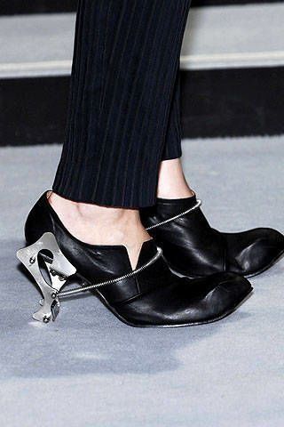 Close up of black shoes with unique metal heels and pleated pants
