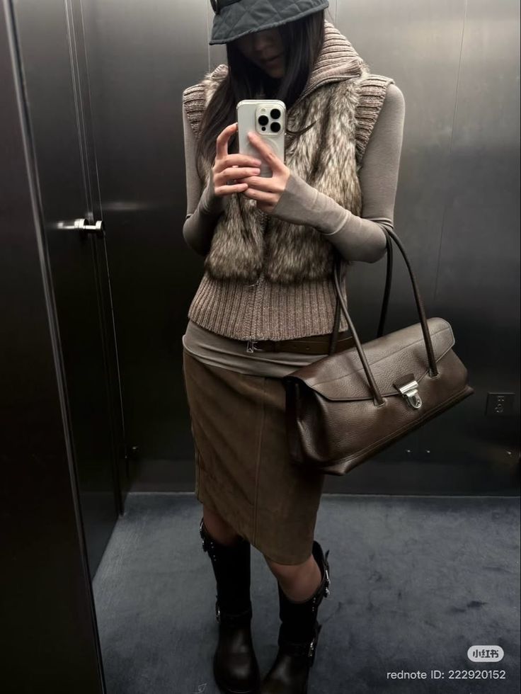 Person in a fur vest and midi skirt taking a mirror selfie indoors