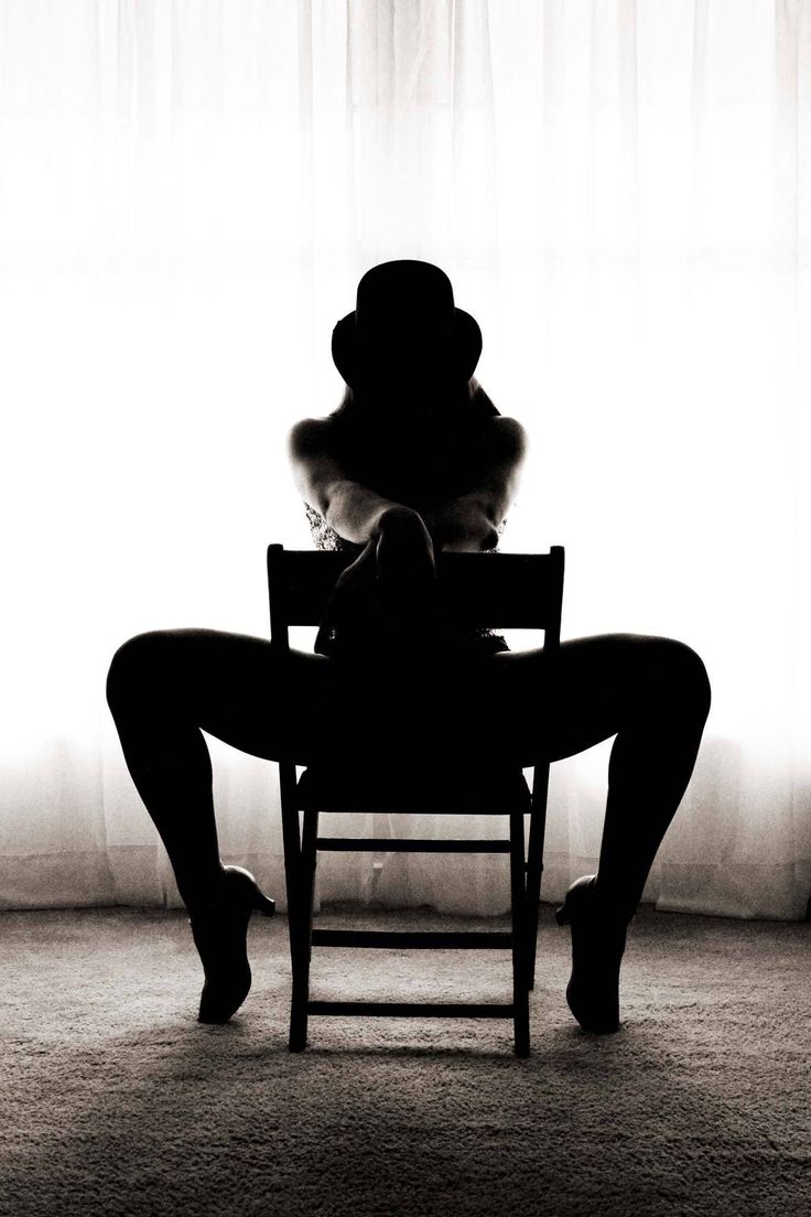 Woman in a top hat and high heels posing in silhouette against a bright window