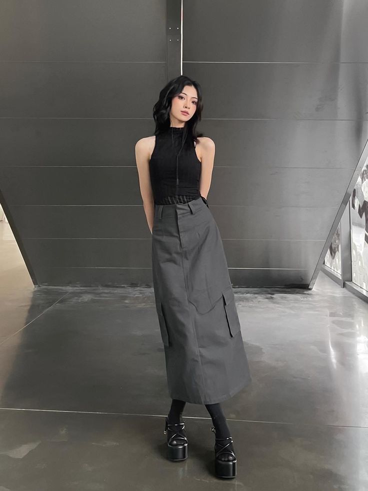 Woman with black hair wearing a black top and cargo skirt with platform shoes