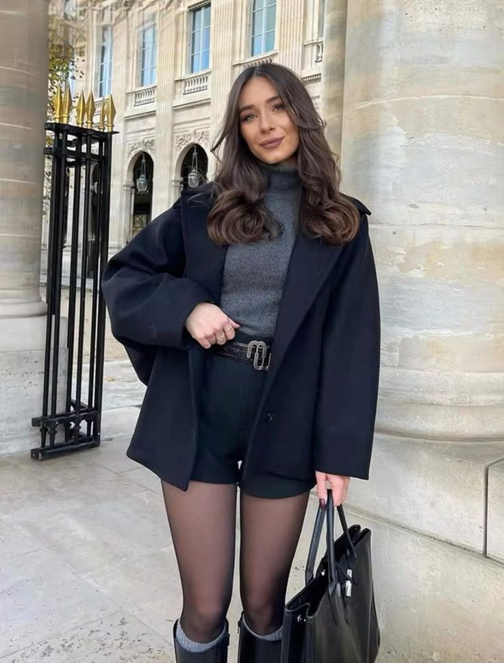 Woman in a black coat and shorts with tights standing outdoors