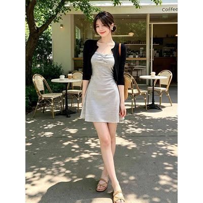 Woman in a light gray dress and black cardigan standing outside a cafe