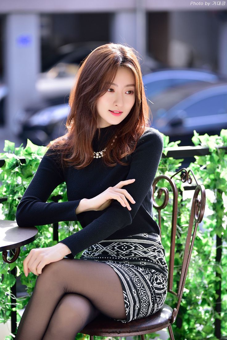 Woman with long hair wearing a black turtleneck and patterned skirt, sitting outdoors