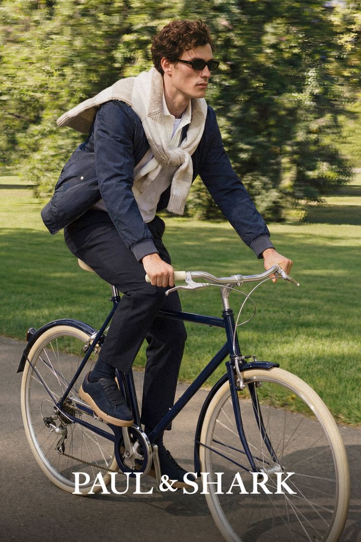 Man with curly hair and sunglasses riding a bicycle in a park