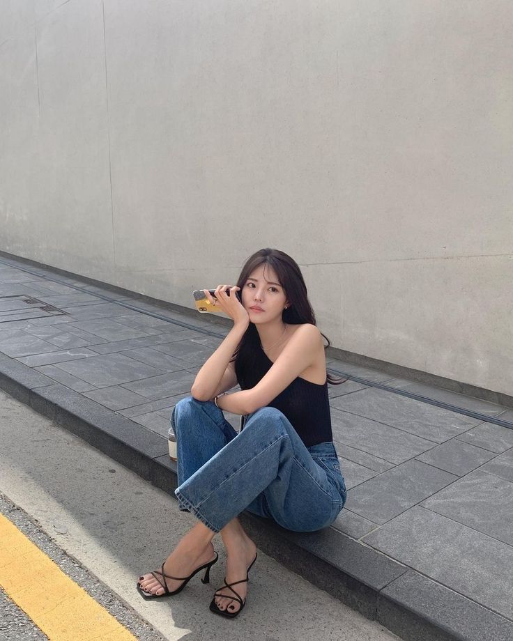 Woman with long hair sitting on a curb in jeans and a black top