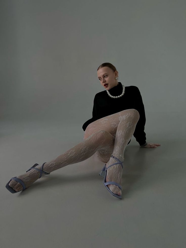 Woman in a black turtleneck and white lace tights posing in a studio