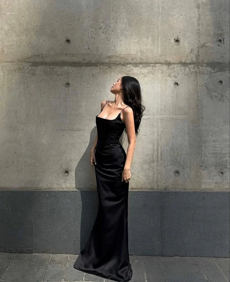 Woman in a black slip dress posing against a concrete wall in dramatic lighting