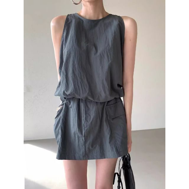 Woman in a gray sleeveless dress with a black bag and hoop earrings