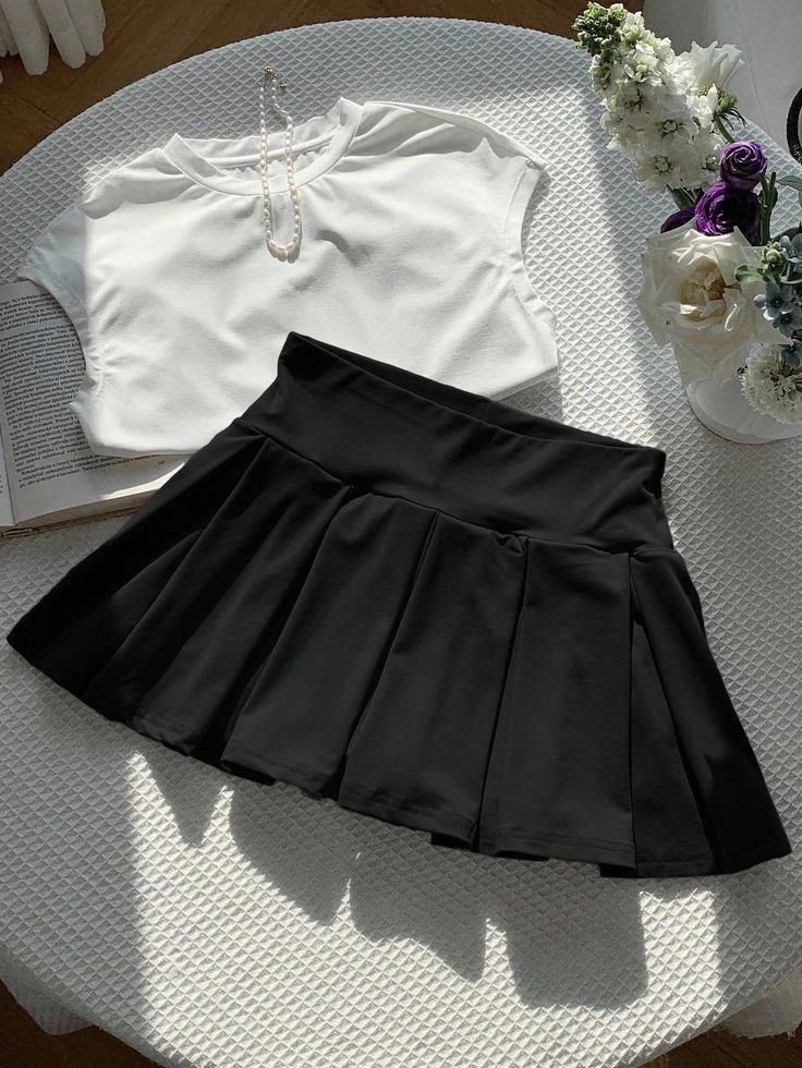 Black pleated skirt and white top with a pearl necklace on a table