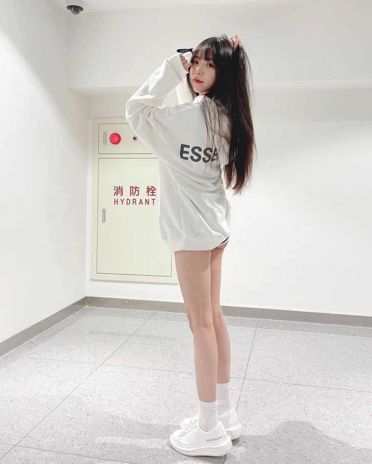 Woman in a white sweatshirt and white sneakers posing indoors