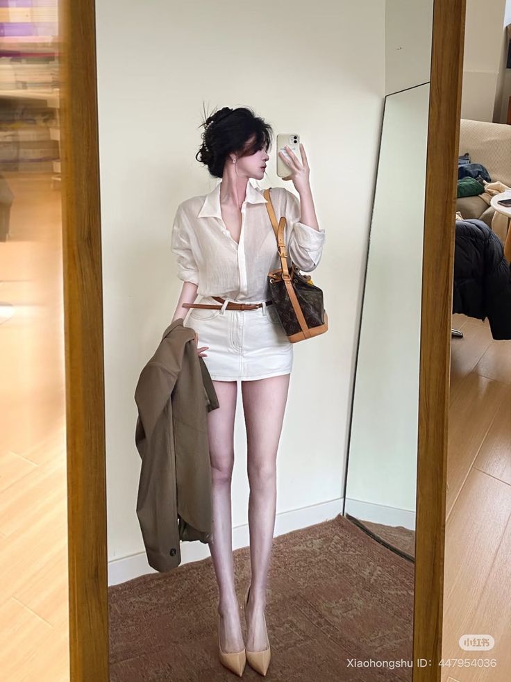 Woman in a white shirt and mini skirt taking a mirror selfie