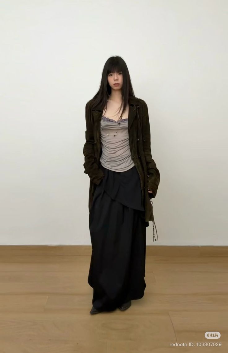 Woman with long dark hair wearing a dark coat and black skirt indoors